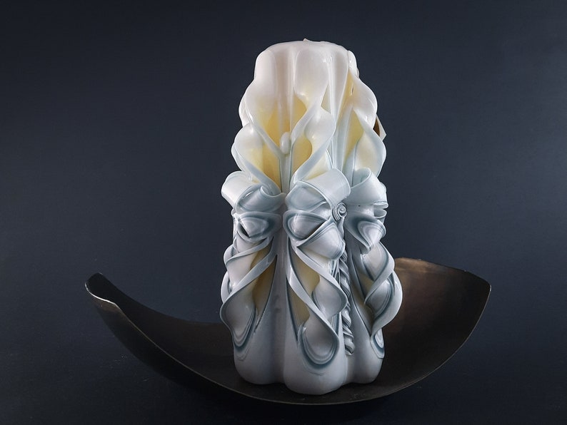 May include: A white and blue carved candle with intricate details. The candle is sitting on a dark brown metal plate.