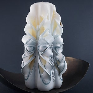 May include: A white and blue carved candle with a decorative design. The candle is sitting on a dark brown surface.