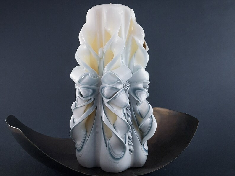 May include: A white and blue carved candle with a decorative design. The candle is sitting on a dark brown surface.