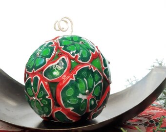 May include: A green and red Christmas bauble with a leaf pattern. The bauble is decorated with silver glitter and is sitting on a silver tray.