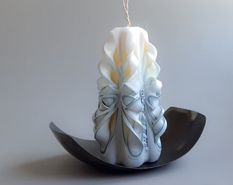 May include: A white and blue carved candle with a decorative design. The candle is sitting on a black metal plate.