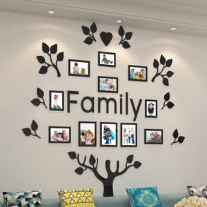 Può includere: Un set di decorazioni murali nere con la scritta "Family" e diverse foto incorniciate. Il set include accenti di foglie e cuori neri, creando un design ad albero. Le cornici contengono varie foto di famiglia.