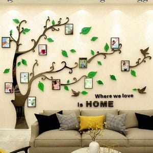 May include: Wall decoration with a tree design, photo frames, green leaves, and bird silhouettes. The words "Where we love is HOME" are displayed. A beige sofa with cushions and a marble coffee table complete the scene.