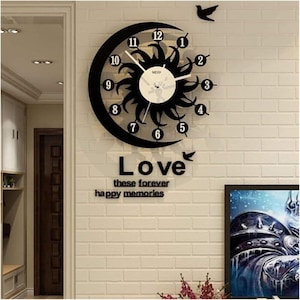 Puede incluir: Un reloj de pared en blanco y negro con un diseño de sol y forma de media luna. El reloj tiene los números del 1 al 12. Las palabras "Love, these forever, happy memories" están debajo. También se incluyen dos siluetas de pájaros.