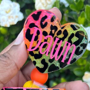 May include: A pink, green, and orange heart-shaped keychain with a black leopard print and the name "Dawn" written in pink letters.