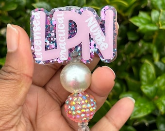 Puede incluir: Portagafete de purpurina rosa con el texto "Licensed Practical Nurse" y un dije de perla blanca y strass iridiscente.