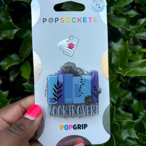 May include: A silver PopSocket PopGrip with a blue and white design of stacked books and the text "Booktrovert".
