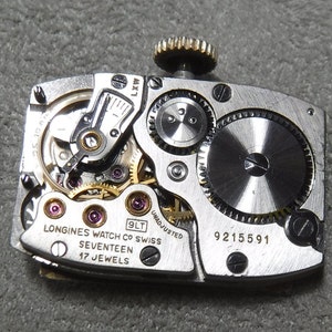 May include: Close-up of the back of a silver Longines watch with a 9LT movement. The watch has a 17 jewel movement and is unadjusted. The serial number is 9215591.