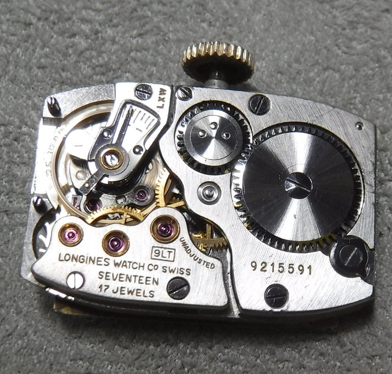 May include: Close-up of the back of a silver Longines watch with a 9LT movement. The watch has a 17 jewel movement and is unadjusted. The serial number is 9215591.