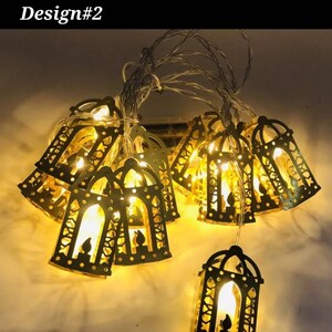 May include: String of lights with 15 gold lanterns shaped like a mosque. The lanterns are illuminated with warm white lights. Design #2.
