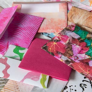 Op de afbeelding: Een verzameling kleurrijke enveloppen met verschillende patronen en ontwerpen. De enveloppen zijn gemaakt van papier en hebben verschillende maten en vormen. Sommige enveloppen hebben een witte achtergrond met een roze, groene en blauwe print. Andere hebben een roze achtergrond met een witte print. Eén envelop heeft een bloemenprint met rode, roze en groene bladeren.