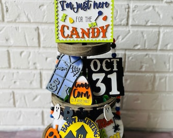 May include: A tiered wooden tray decorated with Halloween-themed signs and decorations. The signs include "I'm just here for the candy", "Oct 31", "Candy Corn is a vegetable right?", "Happy Haunting", and "Trick or Treat".