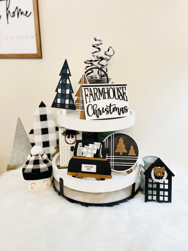 May include: A two-tiered white tiered tray decorated with black and white buffalo plaid and black and white geometric patterned Christmas ornaments. The tray features a sign that reads "FARMHOUSE Christmas".