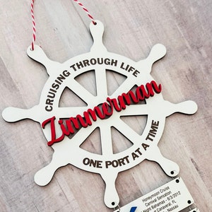 May include: White wooden ship wheel with red text that reads "Cruising Through Life" and "One Port At A Time". The name "Zimmerman" is written in red cursive across the center of the wheel.