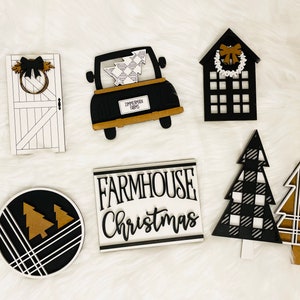 May include: A set of six black and white farmhouse Christmas decorations. The decorations include a truck with a Christmas tree in the back, a house with a wreath on the door, a door with a wreath, a round sign with two Christmas trees, and two Christmas trees with a black and white plaid pattern.