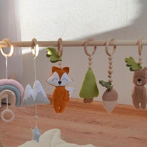 森の吊り下げ式おもちゃで赤ちゃんのプレイジムを彩る：天然木フレーム、森の動物のおもちゃ、葉っぱのマット。森の保育園の装飾