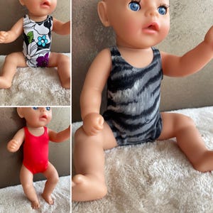 Può includere: Sono mostrati tre costumi da bagno per bambole. Uno è rosso, un altro ha un motivo floreale in bianco e nero e il terzo ha un motivo zebrato nero e grigio. Le bambole sono sedute su una superficie di colore chiaro.