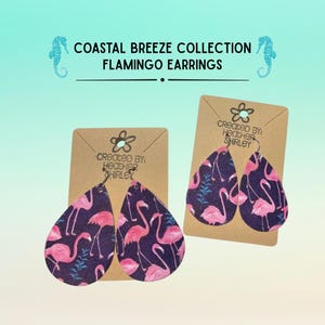 May include: Teardrop-shaped flamingo earrings from the Coastal Breeze Collection. The earrings feature a navy blue background with pink flamingo illustrations. The text "COASTAL BREEZE COLLECTION FLAMINGO EARRINGS" is displayed at the top.