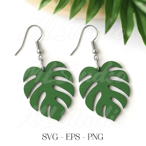 May include: A pair of green, leaf-shaped earrings with silver-colored hooks. The earrings are cut in the shape of a monstera leaf. The image includes the text "SVG - EPS - PNG" at the bottom.