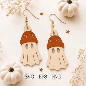 May include: A pair of dangle earrings featuring light-colored wooden ghost shapes wearing burnt orange beanies. The earrings have gold-toned metal hooks and are displayed with small orange star cutouts. The text SVG - EPS - PNG is visible.