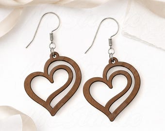 May include: A pair of wooden heart-shaped earrings with a cutout design. The earrings are a warm brown color and hang from silver-colored ear wires. The image includes the text "SVG - EPS - PNG".