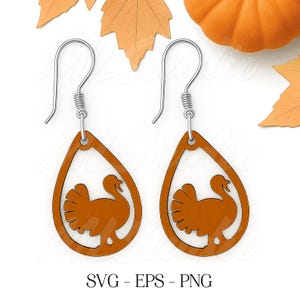 May include: A pair of wooden teardrop earrings with a turkey silhouette cutout. The earrings are a warm brown color and have silver-colored ear wires. The text "SVG - EPS - PNG" is at the bottom of the image.