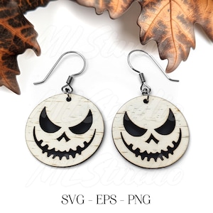 May include: A pair of wooden earrings with a white background and a black jack-o'-lantern face cutout. The earrings are attached to silver hooks.