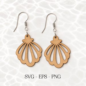 Op de afbeelding: Een paar houten oorbellen in de vorm van een zeeschelp met zilverkleurige oorhaken. De oorbellen zijn lichtbruin met een waaiervormig ontwerp. De tekst "SVG - EPS - PNG" is ook inbegrepen.