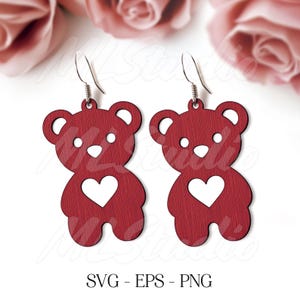 May include: Red wooden bear earrings with a white heart cutout. The earrings are hanging from silver hooks.