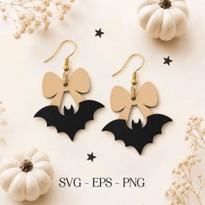 May include: A pair of dangle earrings featuring a beige wooden bow shape attached to a black wooden bat silhouette. The earrings have gold-toned metal hooks. The text SVG - EPS - PNG is printed in black at the bottom center of the image.