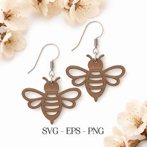 May include: Two wooden bee-shaped earrings with silver hooks. The earrings are light brown and have cut-out details for the wings and body. The image also includes the text "SVG - EPS - PNG".