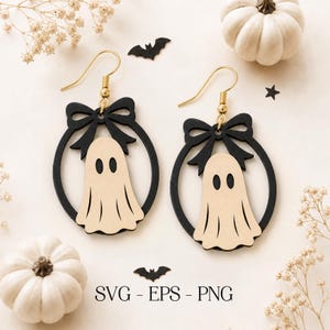 May include: A pair of dangle earrings featuring a beige ghost silhouette centered within a black circular frame topped with a black bow. The earrings have gold-toned metal hooks. The text SVG - EPS - PNG is printed at the bottom center.