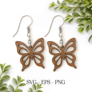 May include: A pair of wooden butterfly earrings with silver-colored hooks. The earrings are a warm brown color and feature a cutout design. The image also includes the text "SVG - EPS - PNG".