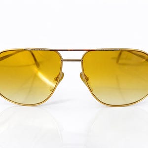 May include: Gold-framed aviator sunglasses with gradient yellow lenses. The sunglasses have a double bridge and a classic teardrop shape. The lenses transition from a darker yellow at the top to a lighter yellow at the bottom.