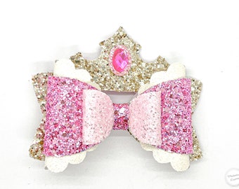 May include: A pink and gold glitter bow with a gold glitter crown and a pink gem in the center.