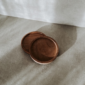 Peut inclure: Deux sous-verres ronds en bois, l'un empilé sur l'autre, sur une surface en béton gris.