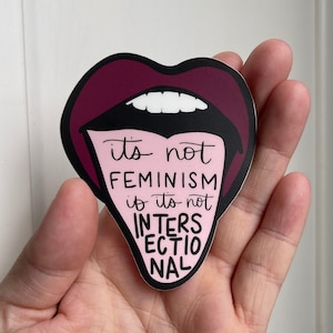 May include: A pink and black sticker with a cartoon mouth and tongue. The tongue says "it's not feminism if it's not intersectional".