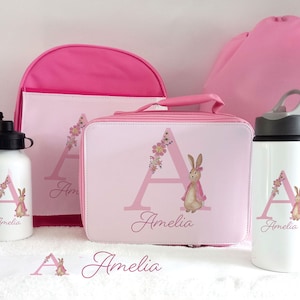 May include: Pink personalised school set with a backpack, lunch bag, two water bottles, and a bean bag. The set features a pink bunny with a floral design and the letter "A" with the name "Amelia" on each item.