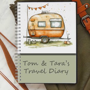 May include: A spiral-bound notebook featuring a watercolour illustration of an orange camper with a banner. The cover displays the text "Tom & Tara's Travel Diary". A brown leather strap and a green bag are visible beside the notebook.