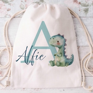 May include: A white drawstring bag with a blue letter A and the name Alfie printed on it. A green dinosaur with a light blue belly is on the bag.