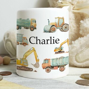 May include: White ceramic mug decorated with illustrations of construction vehicles, such as trucks and excavators. The name "Charlie" is printed in black. A practical and fun item for children.