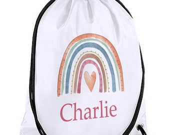 May include: White drawstring bag with a colorful rainbow design and a red heart in the center. The name "Charlie" is printed in pink below the rainbow.