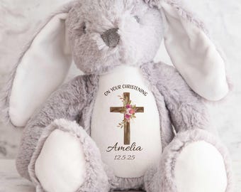 May include: Gray plush bunny with a white cross and floral design on its chest. The cross has the text "On Your Christening" above it and the name "Amelia" and the date "12.5.25" below it.