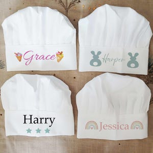 May include: Four white chef hats, each personalised with a name and design. One hat features "Grace" with ice cream cones, another "Harper" with bunny silhouettes. "Harry" is on a hat with stars, and "Jessica" is on one with a rainbow.