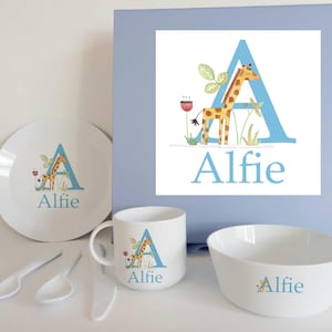 May include: A blue and white children's dinner set featuring a giraffe and the letter A. The set includes a plate, bowl, cup, and two spoons. The name Alfie is printed on each piece.