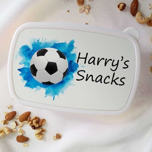 May include: White lunchbox with a blue watercolour background and a black and white football. The text "Harry's Snacks" is printed on the lunchbox.