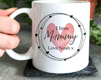 May include: White ceramic mug with a black and pink design. The design features a heart with the words "I love Mummy" and a circle of hearts around it. The text "Love Noah x" is below the heart.