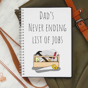 May include: A white notebook with a black spiral binding. The cover has the text "Dad's Never Ending List of Jobs" and a cartoon illustration of a toolbox with tools.