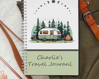 May include: A spiral-bound notebook with a green and white cover featuring a camper illustration in a forest setting. The text "Charlie's Travel Journal" is displayed on the bottom. The notebook is open, revealing the spiral binding.