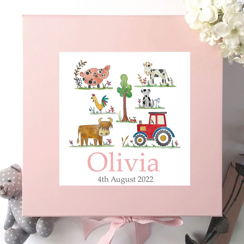 May include: Pink keepsake box with a white label featuring a farm scene with a pig, cow, rooster, dog, tractor, and a brown cow. The label also includes the name Olivia and the date 4th August 2022.